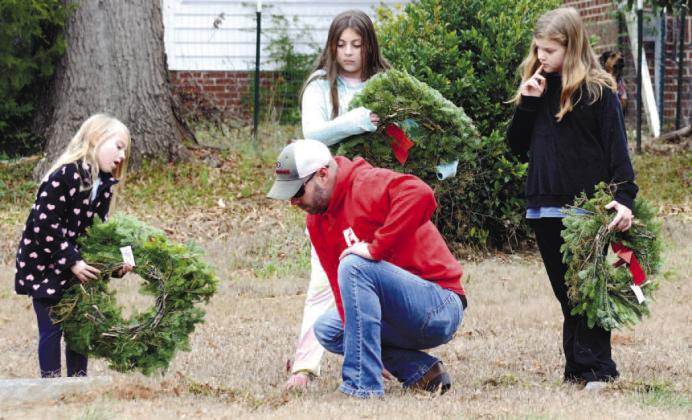 Jason Riddle clears dirt and grass from a veteran’s marker at Eatonton’s Pine Grove Cemetery, as daughters Tiffany and Teagan watch, along with their cousin Rachel Paul (right). IAN TOCHER/Staff