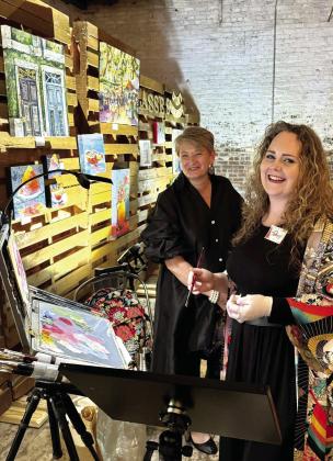 Shannon Minchey, manager of The Artisans Village Gallery stands with artist, Meagan Thomas, as she does a painting demo at the Artisans Market in the Livery during ArtiGras. EMMA CLAUSE/Staff