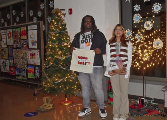 Posing in front of Christmas trees representing PCHS student organizations, graphic design students Scarlett Monje (11th grade) and Tavion Davis (12th) showcase items they designed in class and sold at the silent auction.