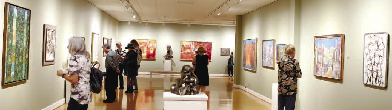 Patrons studying the art of Jack Stewart as part of the Mentor and Protege exhibit at the Steffen Thomas Museum of Art.