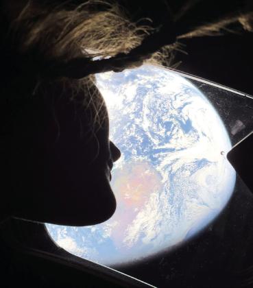 With her hair floating in near-zero gravity, NASA Mission Specialist Christina Koch gazes out at Mother Earth from a window on the Artemis II spacecraft. CONTRIBUTED