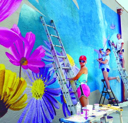 Painters work on a new mural in downtown Eatonton during the Dairy Festival, bringing color to the side of the building that houses Nails by Aaron at the corner of North Jefferson Avenue and Marion Street. IAN TOCHER/Staff