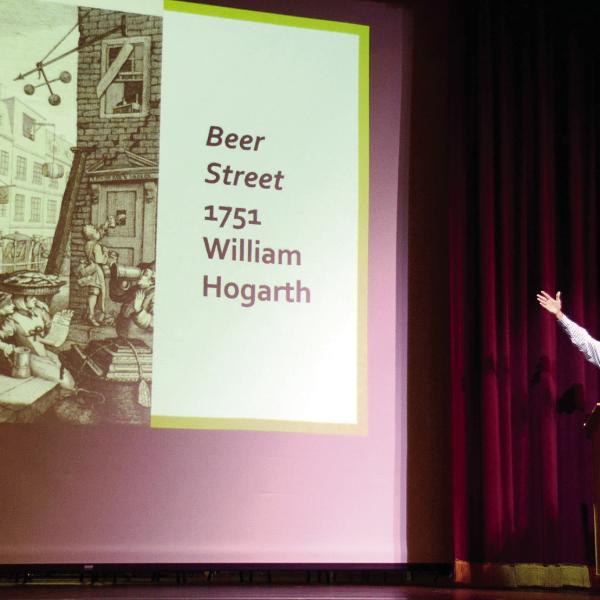 GCSU’s Dr. Eric Tenbus gestures toward the “Beer Street” political cartoon of artist William Hogarth during his talk at The Plaza Arts Center on Sunday afternoon. IAN TOCHER/Staff