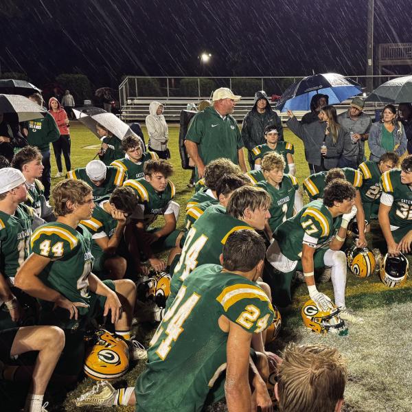 With steady rain falling, Gatewood head coach Jeff Ratliff (right, black jacket) addresses his team at midfield after a disappointing 30-17 loss last Friday to the visiting Windsor Academy Knights, from Macon.