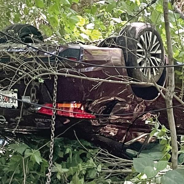 A chain hangs from the overturned Nissan as Hurt’s Towing prepares to remove it from the woods at the end of East Sumter Street Monday. LYNN HOBBS/ Staff