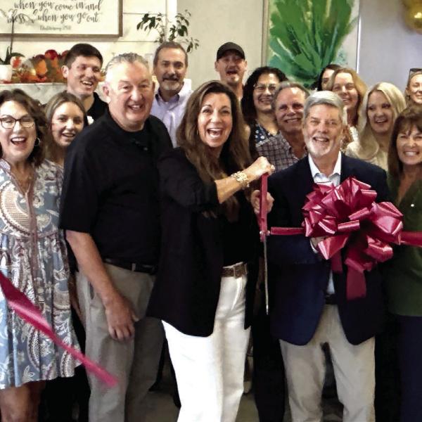 With husband Steve at her back, Compassion Café owner Lisa Tubbs wields the scissors for a ribbon-cutting ceremony arranged by Robbie King (behind bow) of the Eatonton-Putnam Chamber of Commerce. IAN TOCHER/Staff