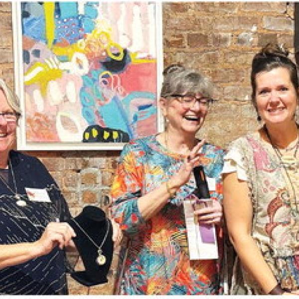 L-R: Art show chairperson Michele Hartung and co-chair Cathy McIntire congratulate The Artisans Village communications specialist Melanie Schneider after she won a Merit Award for “Golden Spiral,” a necklace she designed and created. IAN TOCHER/Staff