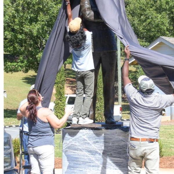 Nikki Barker (left) of the Eatonton Veterans Thrift Store, helps workers temporarily cover up the statue of Hiram Little.