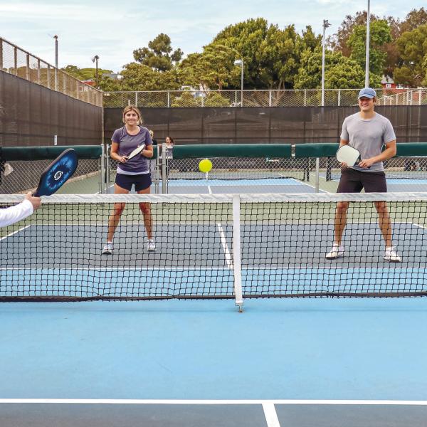 Dedicated pickleball courts appear like mini tennis courts, while the rackets look like oversized ping-pong paddles. The ball itself is plastic with holes throughout, similar to what’s commonly known as a whiffle ball. Mixed doubles (shown) is a very popular team option for the socially oriented sport. CONTRIBUTED