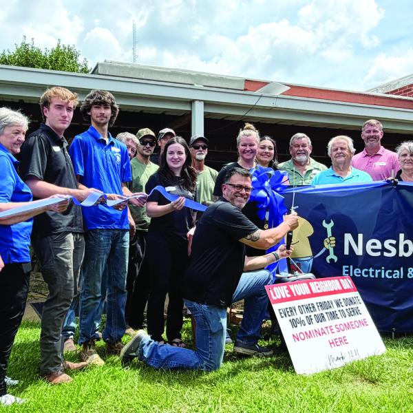 Carlos Campos (kneeling) prepares to cut the ribbon July 10, to officially reopen Nesbitt Repair, an existing business that he and his wife, Chantel, purchased early this year from its founder, Frank Nesbitt. SKYLA MORRIS/Staff
