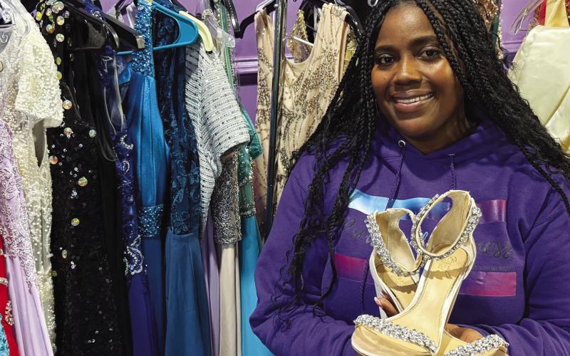 Reasha Daniels of Pretty Girlz Fitness in downtown Eatonton poses with just a few of the more than 200 formal dresses donated to provide local girls with prom and pageant gowns. IAN TOCHER/Staff