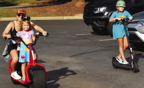 Angela Sauter gives younger daughter Elowen a ride while older sister Hadley rides alongside on an electric scooter. LENA HENSLEY/Staff