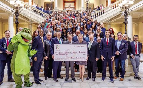 Gov. Brian Kemp (front center) accepts a symbolic $5 billion check from Amanda Dyson-Thornton, executive director of the Georgia Association of Convention &amp; Visitors Bureaus. MMCVB Executive Director Jennifer Rosa León is at top right of the main staircase before it turns right. CONTRIBUTED