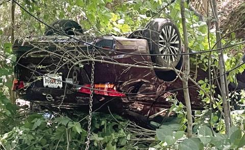 A chain hangs from the overturned Nissan as Hurt’s Towing prepares to remove it from the woods at the end of East Sumter Street Monday. LYNN HOBBS/ Staff