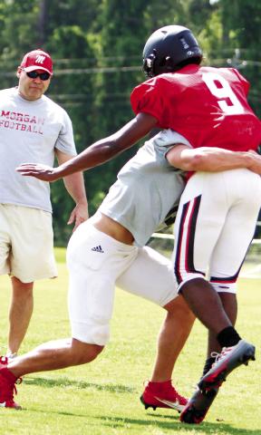 Morgan County head coach Clint Jenkins looks on as two of his players work on making contact during a defensive drill at a practice last week. LANCE McCURLEY/Staff