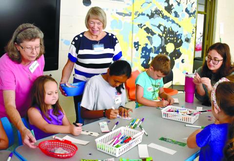 Volunteers Sandra Gunn (left), and Laura Hotzler watch as campers color bookmarks for veterans.