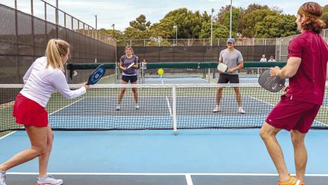 Dedicated pickleball courts appear like mini tennis courts, while the rackets look like oversized ping-pong paddles. The ball itself is plastic with holes throughout, similar to what’s commonly known as a whiffle ball. Mixed doubles (shown) is a very popular team option for the socially oriented sport. CONTRIBUTED