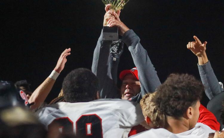 Morgan County head coach Clint Jenkins hoists the trophy as he and players celebrate after defeating Harlem. LANCE MCCURLEY/Staff