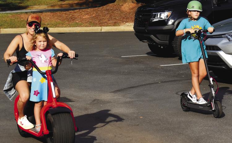 Angela Sauter gives younger daughter Elowen a ride while older sister Hadley rides alongside on an electric scooter. LENA HENSLEY/Staff
