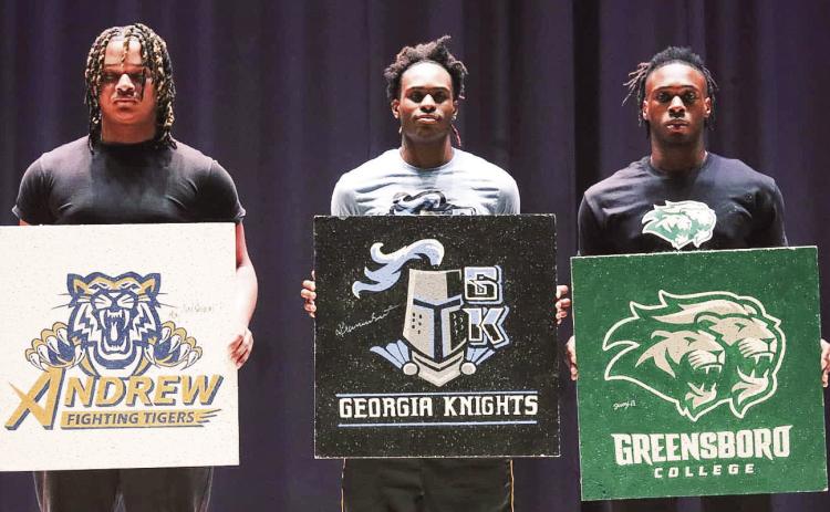 (From L to R): Greene County athletes Jay’shaun Jernigan, Kamari Smith, and Jaquavious Burdette, hold up artwork featuring their colleges during Monday’s signing ceremony. (LANCE MCCURLEY/Staff)