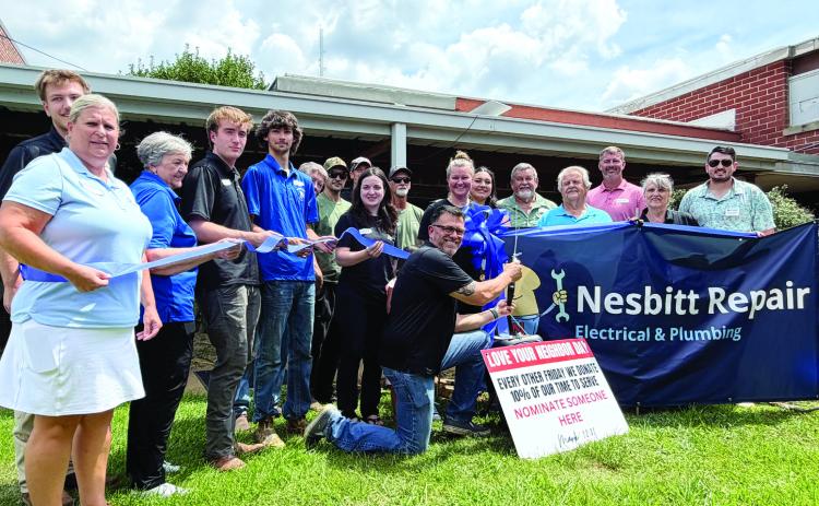 Carlos Campos (kneeling) prepares to cut the ribbon July 10, to officially reopen Nesbitt Repair, an existing business that he and his wife, Chantel, purchased early this year from its founder, Frank Nesbitt. SKYLA MORRIS/Staff